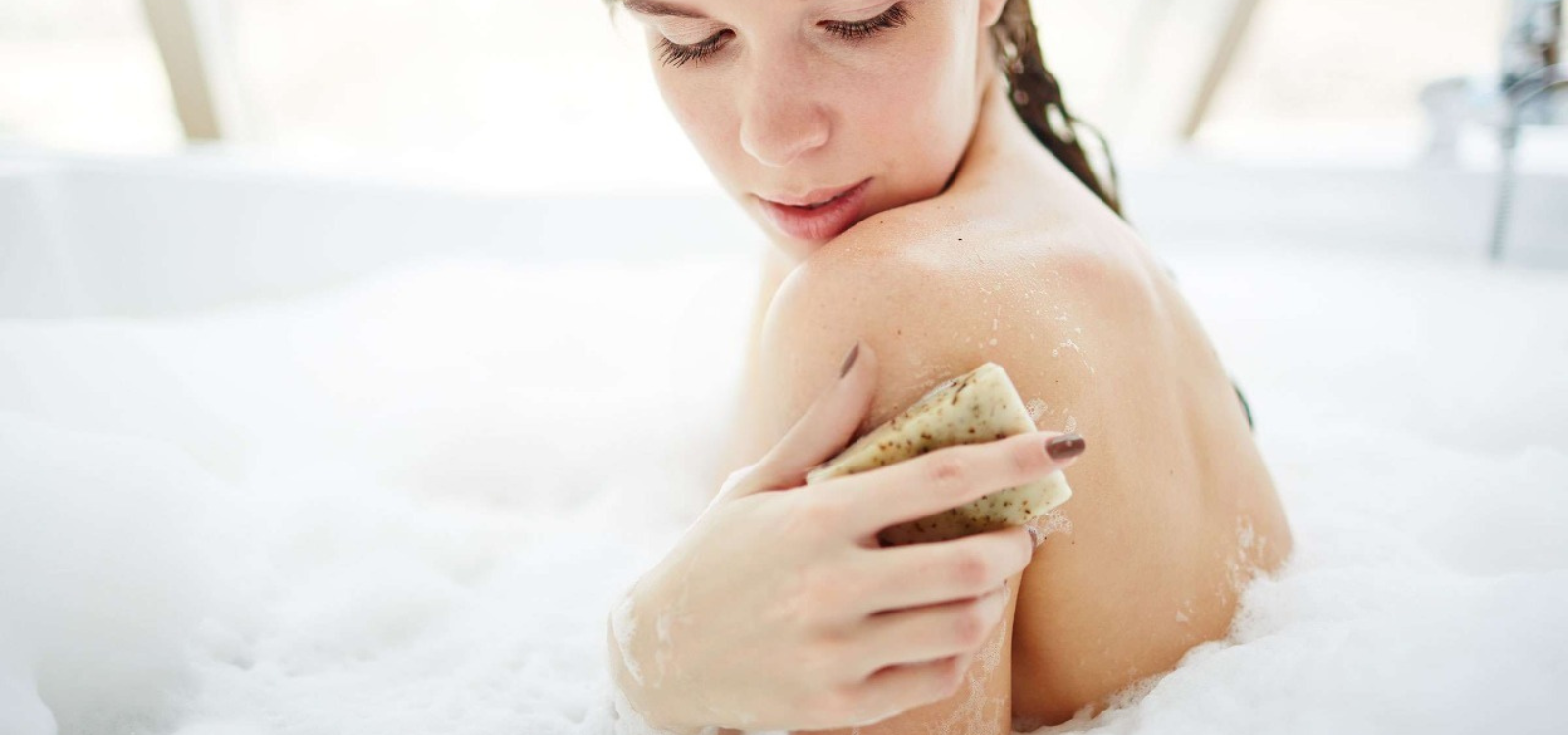 Woman applying cream to her shoulder with a blurred background