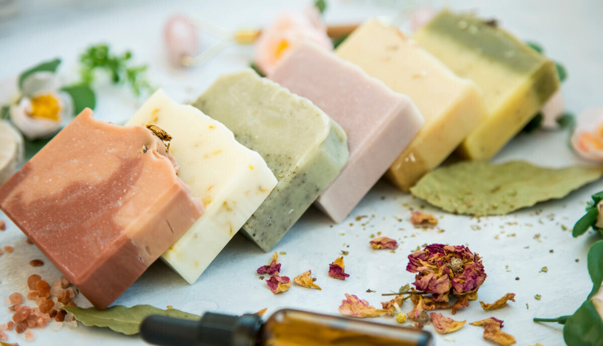 Assorted bars of soap on a textured surface with dried flowers and leaves.